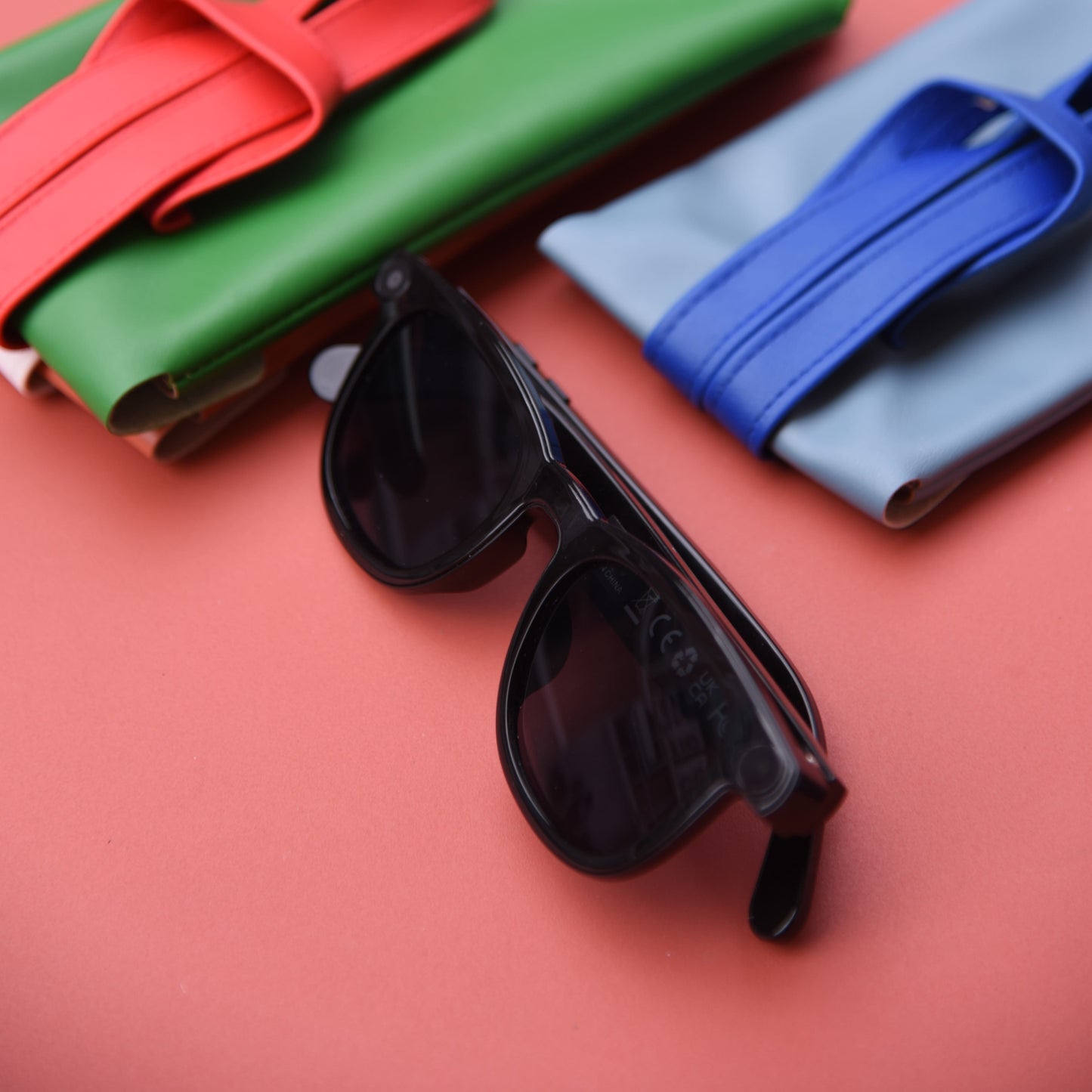 Black sunglasses on a red surface with colorful fabric rolls in the background