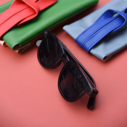 Black sunglasses on a red surface with colorful fabric rolls in the background