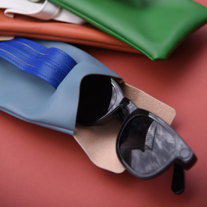 Black sunglasses in a blue case on a red surface with colorful fabric in the background