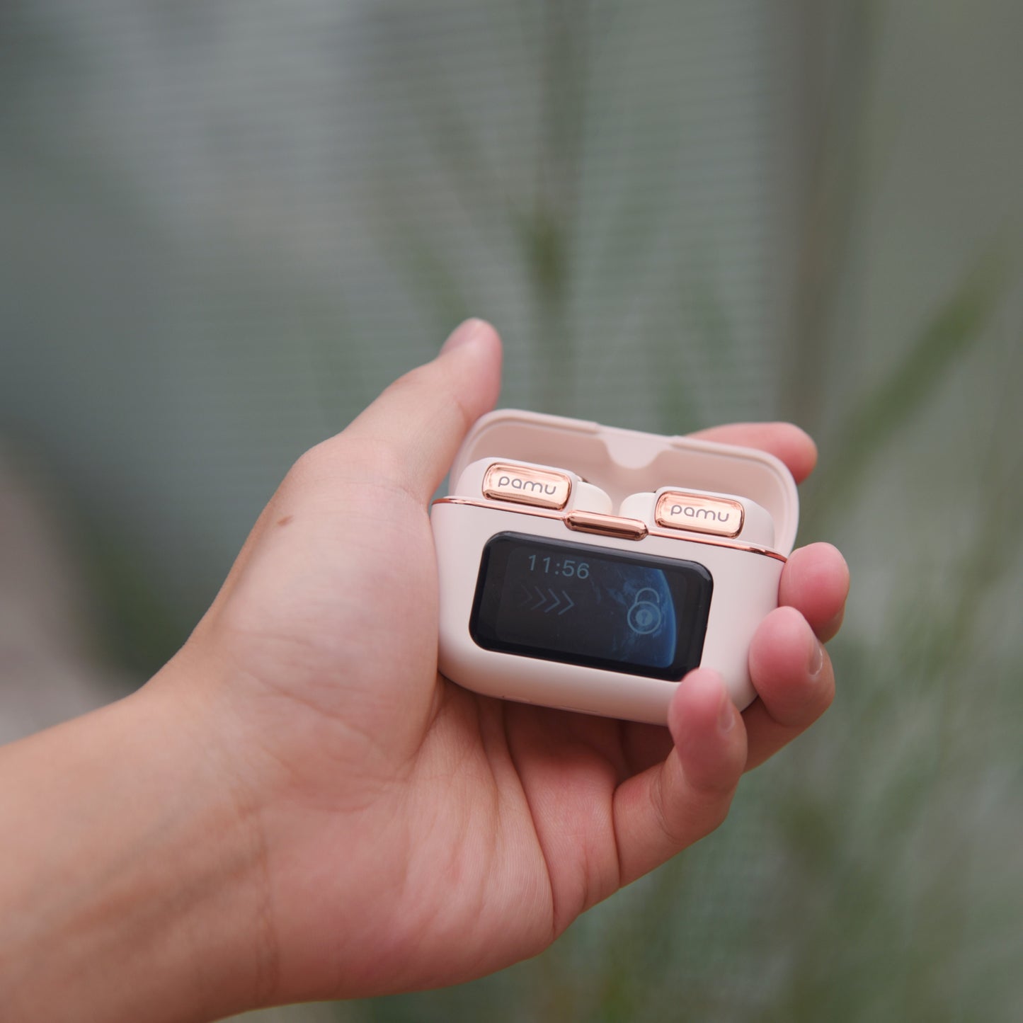 Hand holding a small electronic device with a screen and buttons, against a blurred natural background.